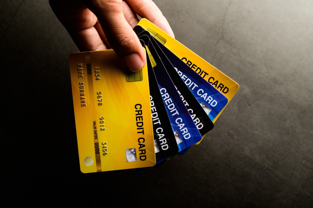 Close-up of a hand holding a fan of multiple credit cards in yellow, blue, and black colors against a dark background. The cards are spread out to display the word ‘CREDIT CARD’ printed on each, symbolizing financial options, consumer credit, and personal finance management.